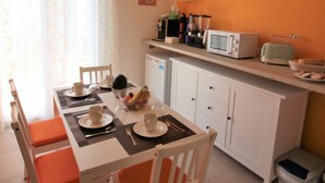 A compact kitchen with white cabinets, a microwave, and a toaster. There is a dining table with orange chairs and a window with curtains. - B&B La Rosatea (Monreale)