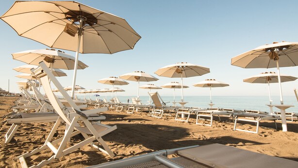 A beach with rows of white lounge chairs and beige umbrellas.