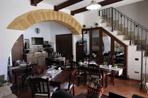 A spacious dining area with a large table and chairs, a kitchen in the background, and a staircase leading to an upper level. - B&B Rabaté (Agrigento)