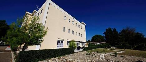 A multi-story building with a flat roof, a covered outdoor area, and a landscaped garden with a gravel pathway.