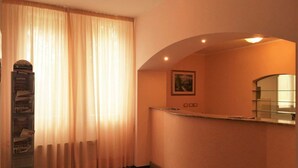 Un espace d’accueil d’hôtel avec un comptoir incurvé, un tableau encadré accroché au mur et un panneau d’affichage où sont affichées diverses informations.
