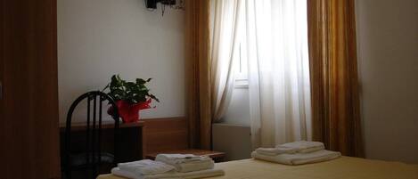 A hotel room with a bed, a TV mounted on the wall, a chair, a small table, and a potted plant.
