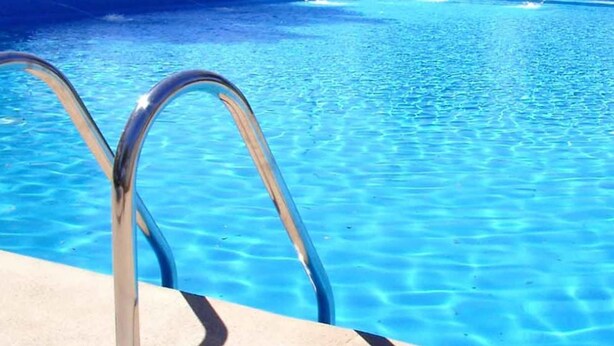 Une piscine à l’eau d’un bleu limpide, équipée d’échelles métalliques.