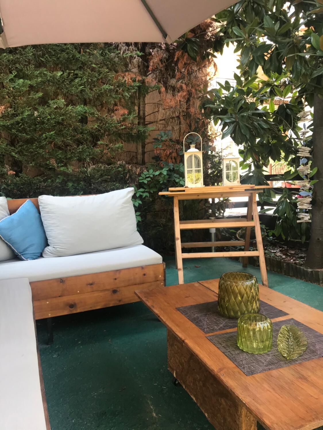 An outdoor seating area with a wooden bench, a white sofa with blue cushions, and two lanterns on a wooden table.