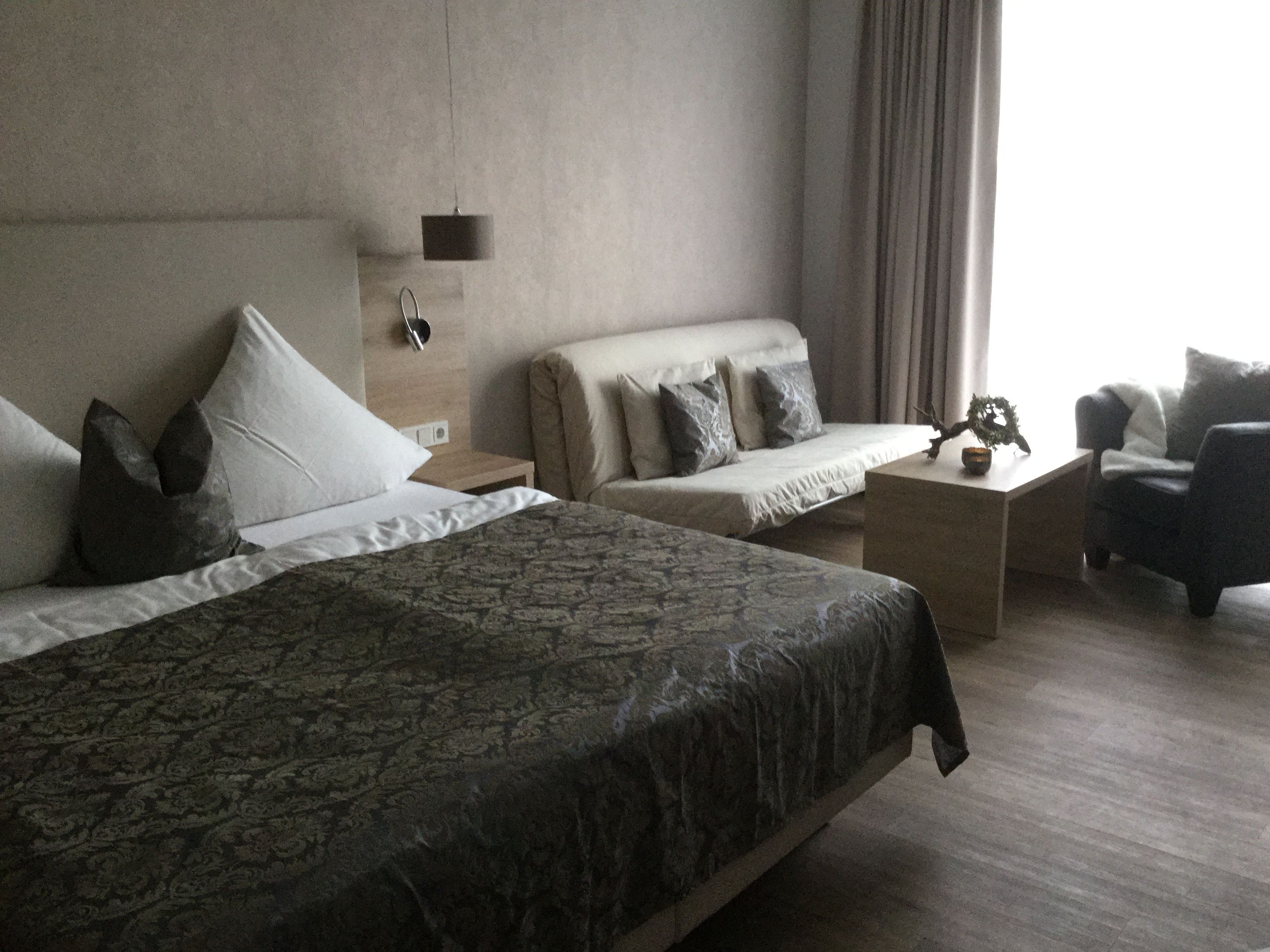 A hotel room with a large bed, a sofa, a chair, and a small table.