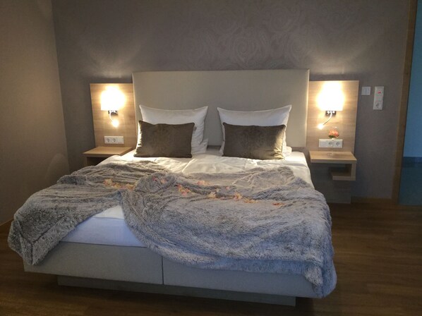 Una cama bien hecha con un edredón esponjoso, dos lámparas de noche y una mesita con un pequeño jarrón de flores.