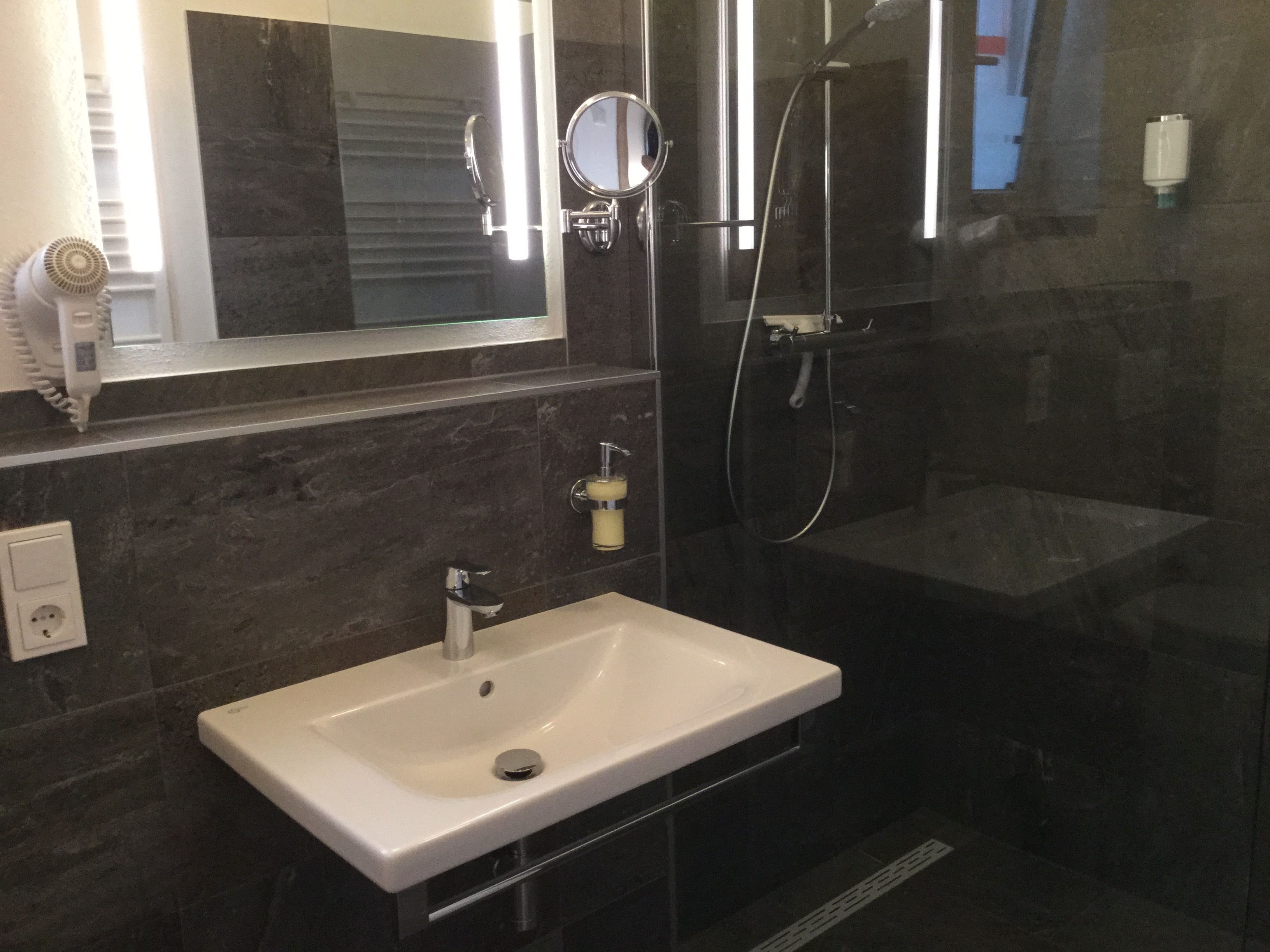 A modern bathroom with a white sink, a handheld showerhead, and a mirror.