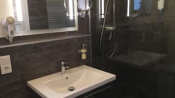 A modern bathroom with a white sink, a handheld showerhead, and a mirror.