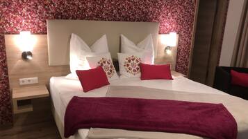 A neatly made bed with white linens, two red pillows, and a purple throw blanket. There are two wall-mounted lamps on either side of the bed.