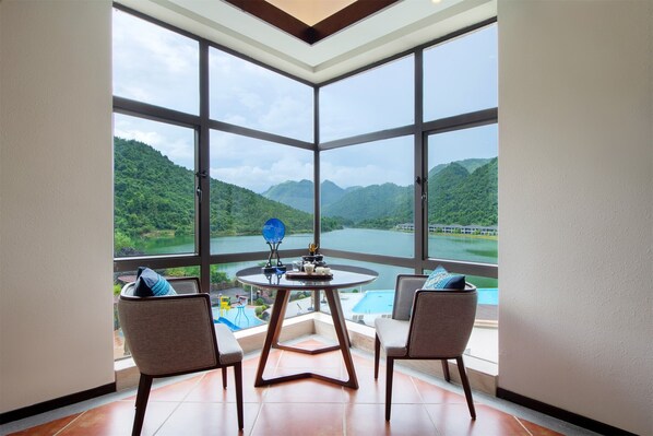 Una habitación con un ventanal grande con vistas a un lago y montañas, una mesa redonda con sillas y una piscina pequeña.