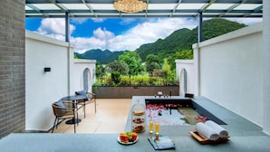 A balcony with a table set for breakfast, a view of mountains, and a pergola structure.
