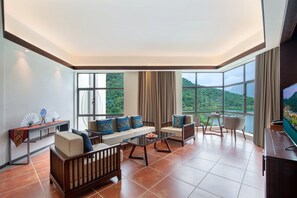 A spacious living room with a sofa set, a coffee table, and a TV. Large windows offer a view of a mountainous landscape. - Lanshanyuan LN Dongfang Hotspring Resort (Shaoguan)