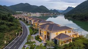A modern hotel with a row of buildings along a curved road, surrounded by lush greenery and a calm river.