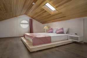A bedroom with a sloped ceiling, a skylight, a bed with a pink bedspread, a nightstand, and a small potted plant.