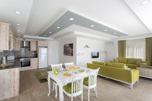 A modern kitchen with white cabinetry, a dining area with a white table and chairs, and a green sofa in the living room.