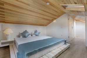 Un dormitorio con techo de listones de madera, una cama con colcha azul y una mesita de noche con lámpara.