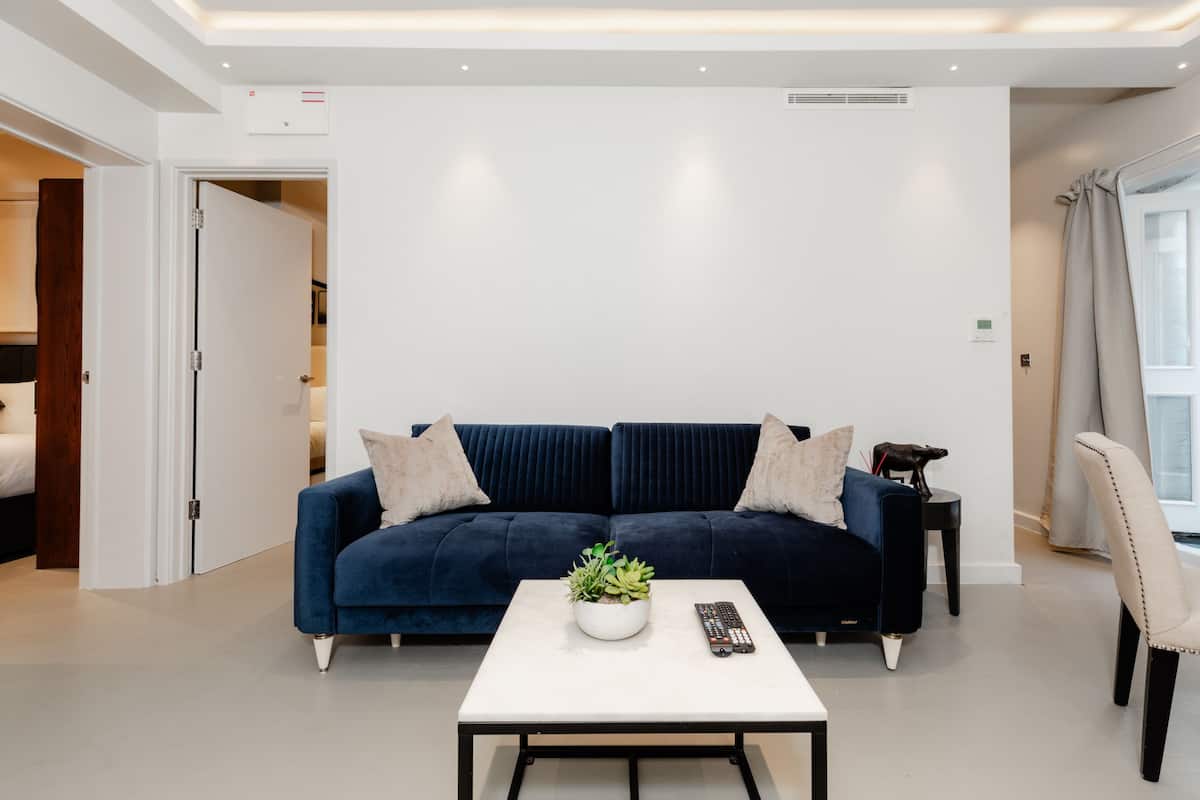 Un salon moderne avec un canapé bleu foncé, une table basse blanche agrémentée d’une plante et une télécommande.