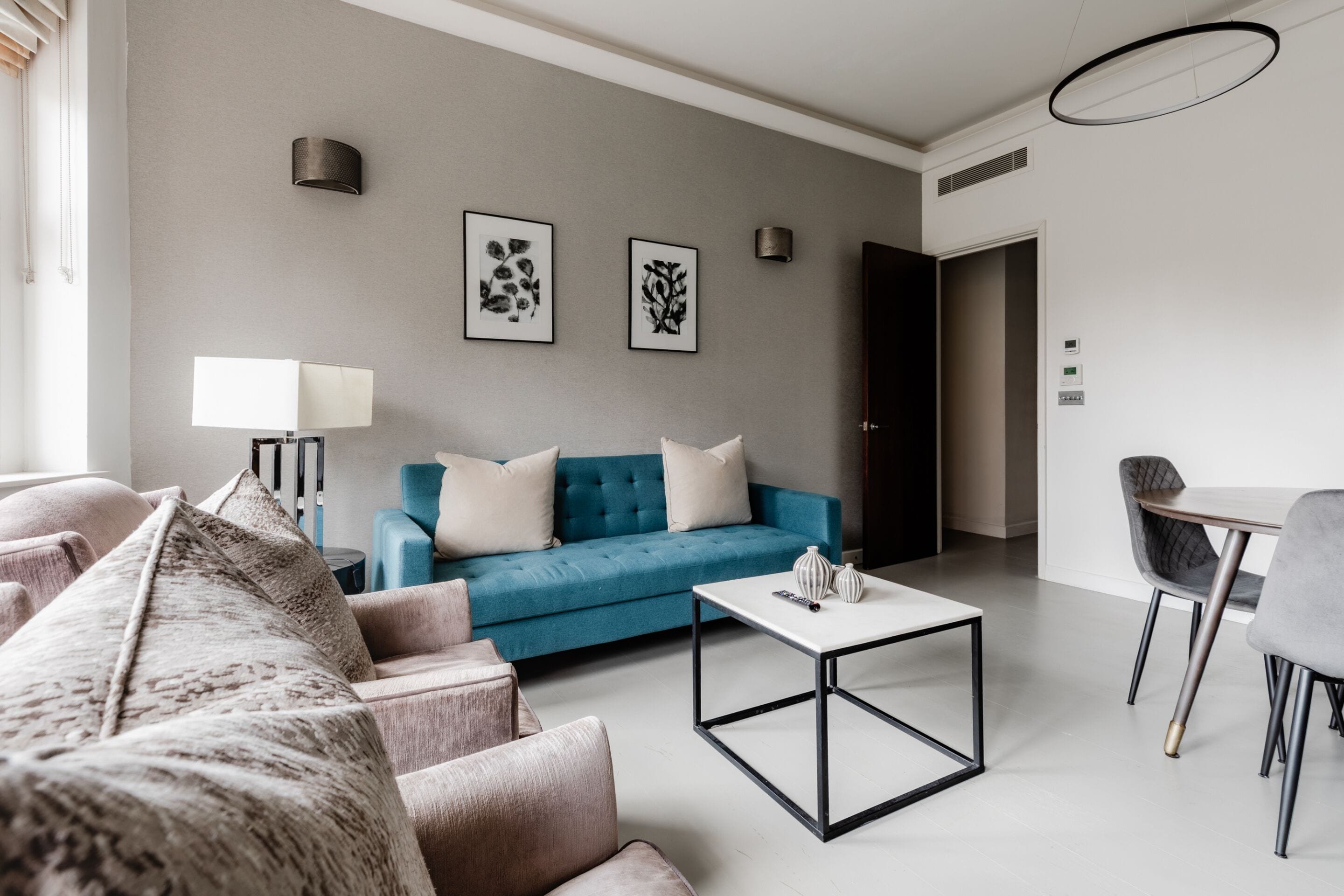 A modern living room with a blue sofa, a white coffee table, and a dining area with a table and chairs.