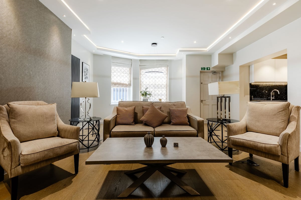 Un salon moderne avec un ensemble de canapés de couleur beige, une table basse centrale et deux petites tables d’appoint avec des lampes.
