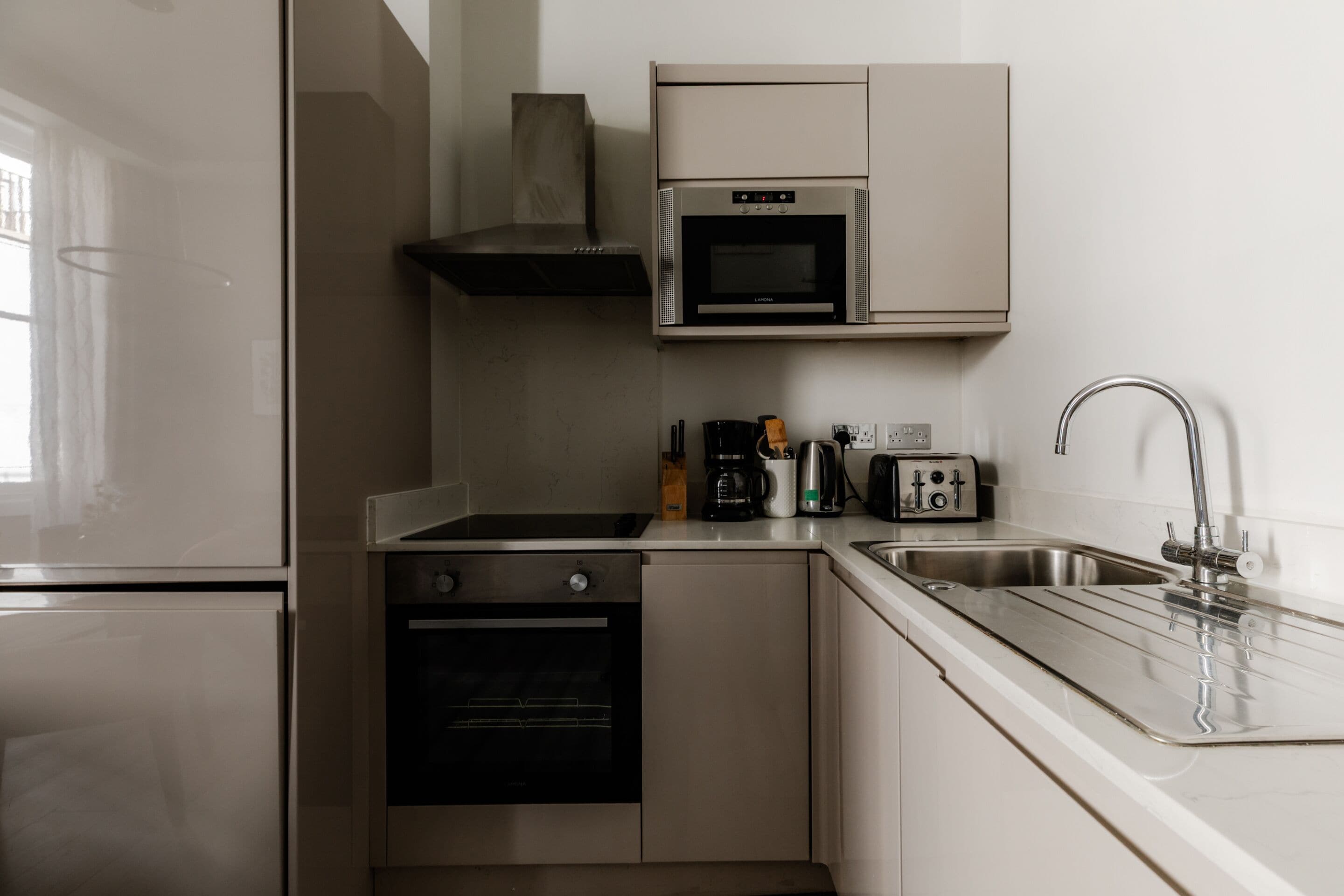Una cocina moderna con electrodomésticos de acero inoxidable, horno integrado, microondas y un lavamanos.