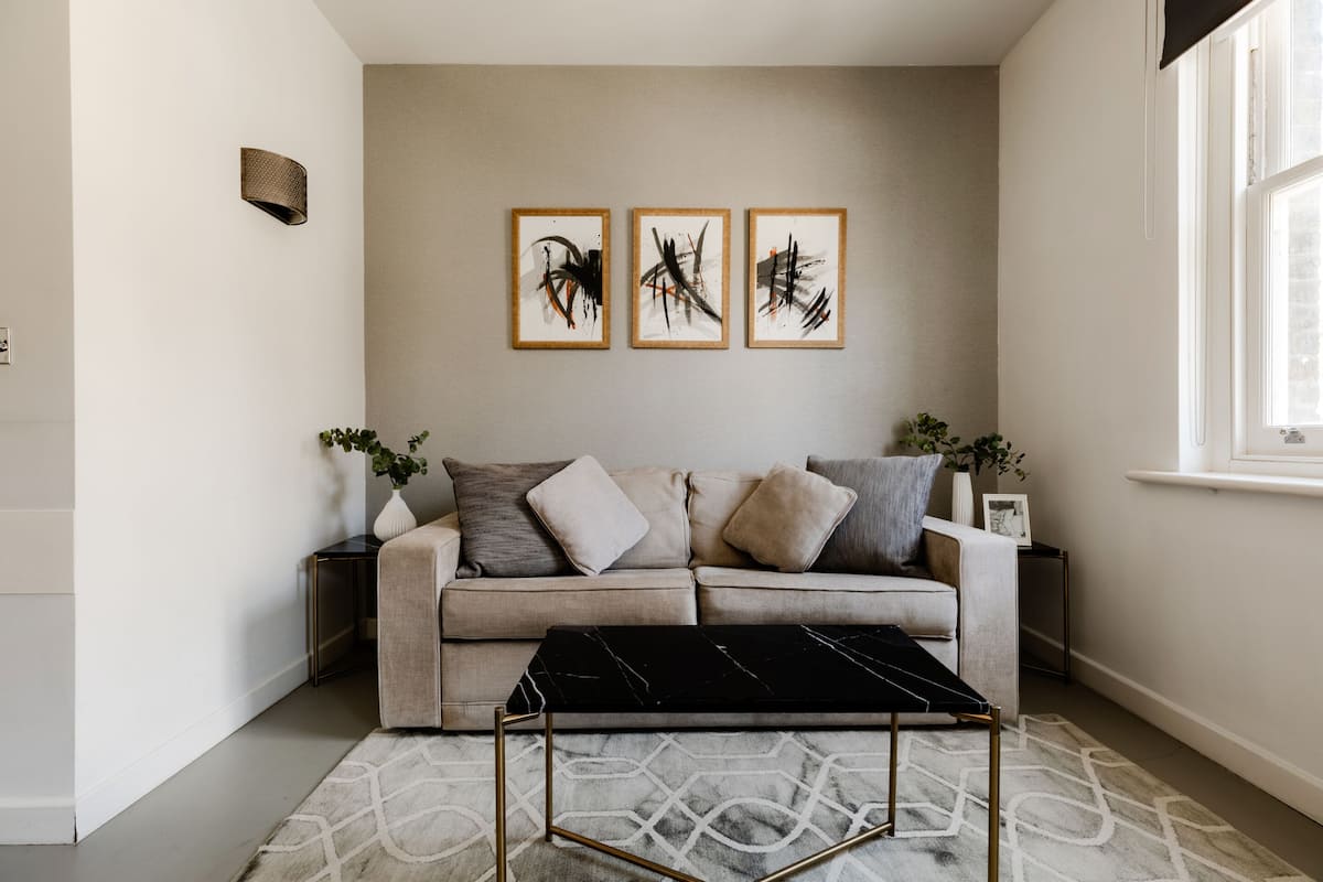 Un salon moderne avec un canapé beige, une table basse en marbre noir et des œuvres d’art abstraites accrochées au mur.