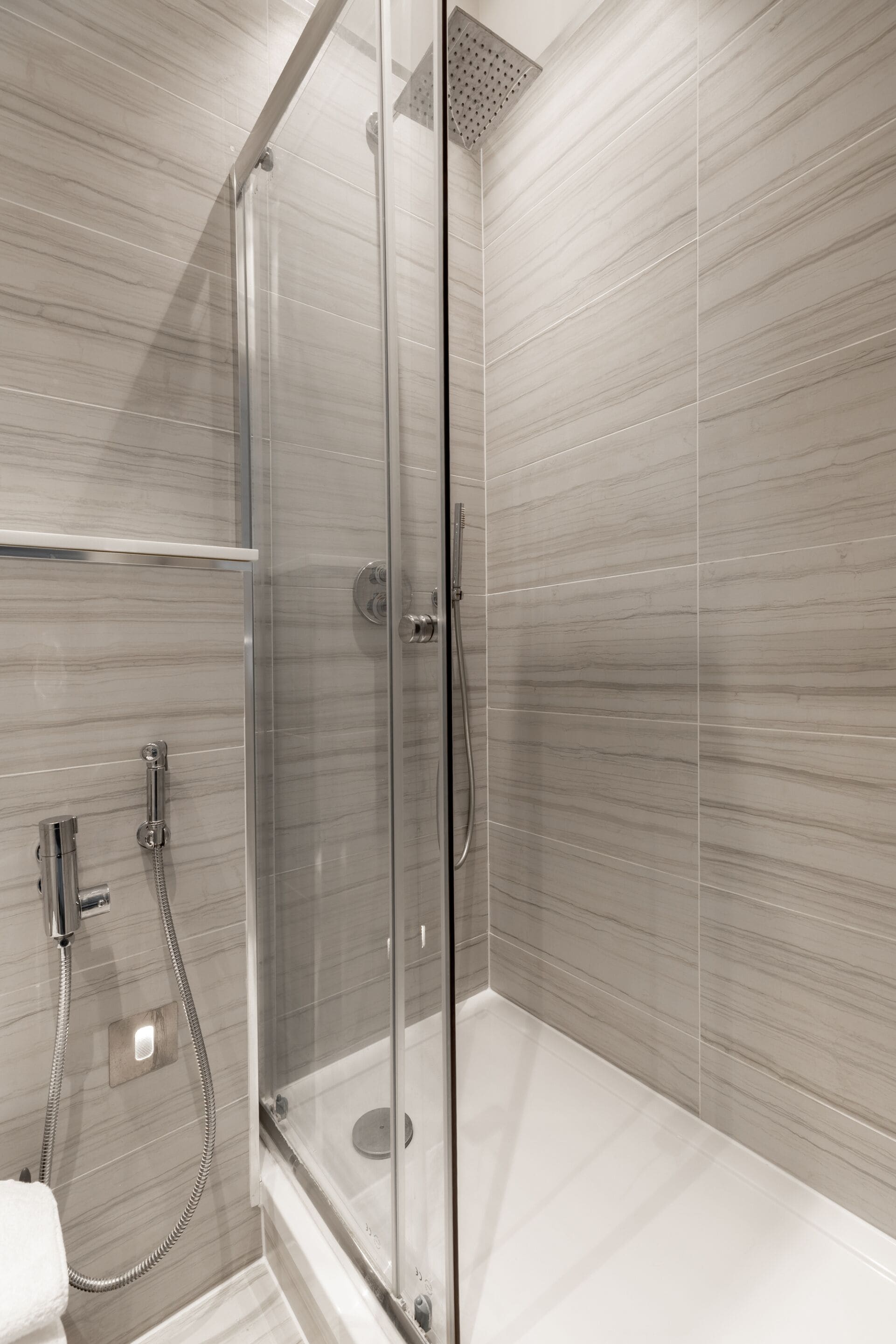 A modern shower area with a glass enclosure, a handheld showerhead, and a wall-mounted faucet.
