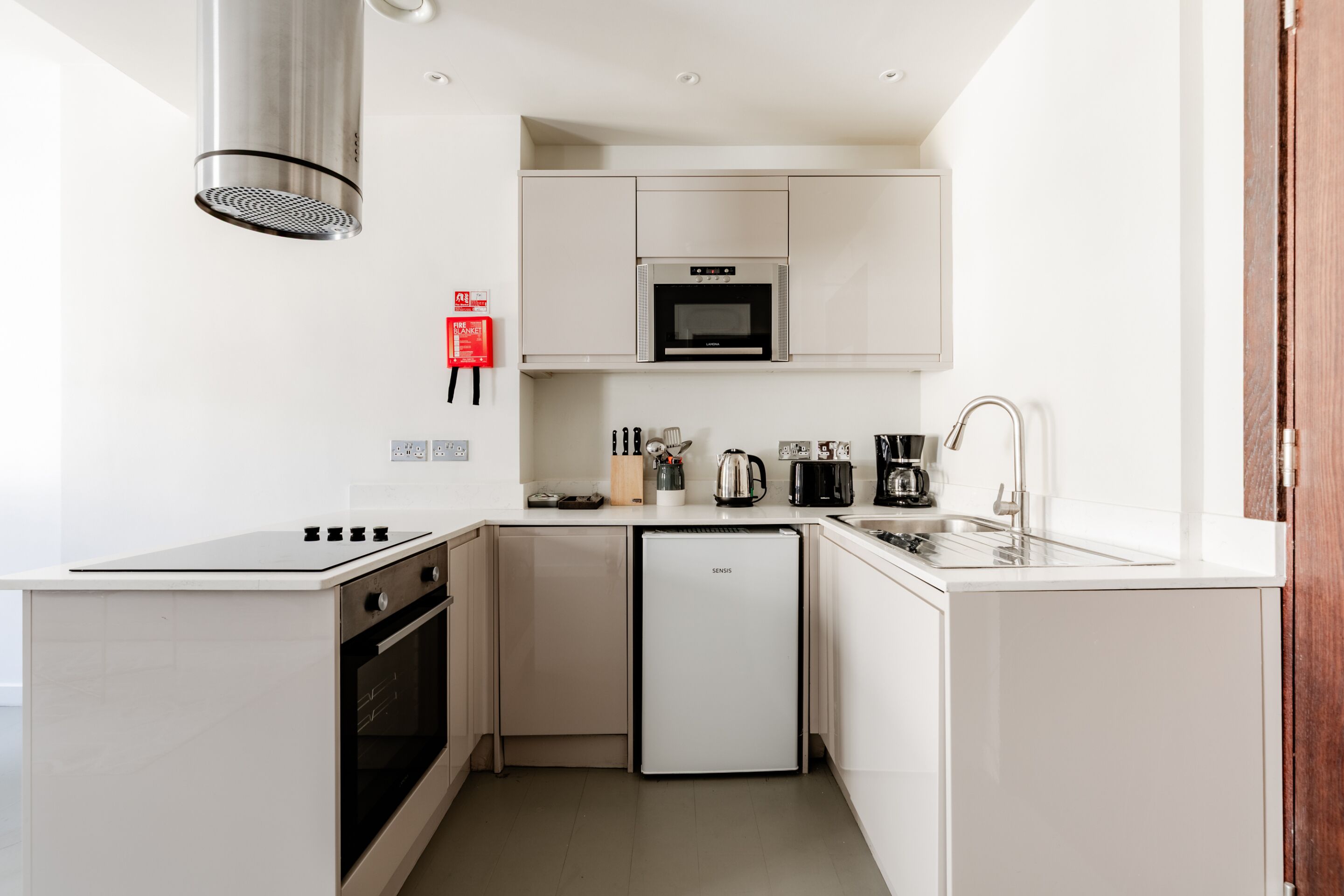 A compact kitchen with white cabinetry, a built-in oven, a microwave, a coffee maker, and a sink.