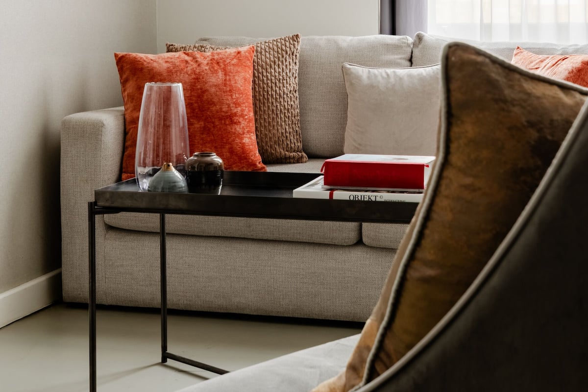 Un salon moderne avec un canapé gris, une table basse noire et un fauteuil marron.