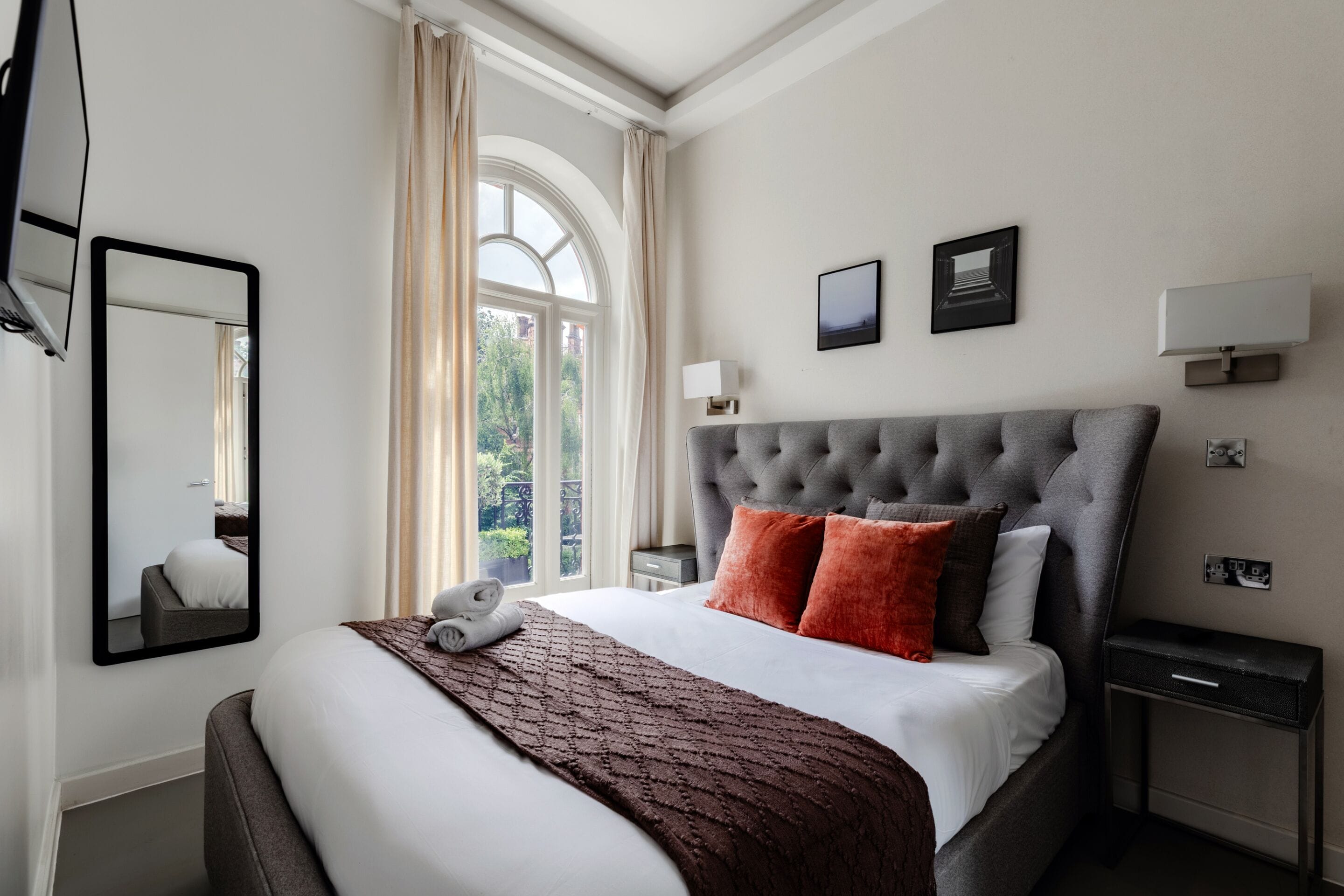 Ein Hotelzimmer mit einem großen Bett, einem Flachbildfernseher, einem Fenster mit Vorhängen, einem Nachttisch und einem Beistelltisch.
