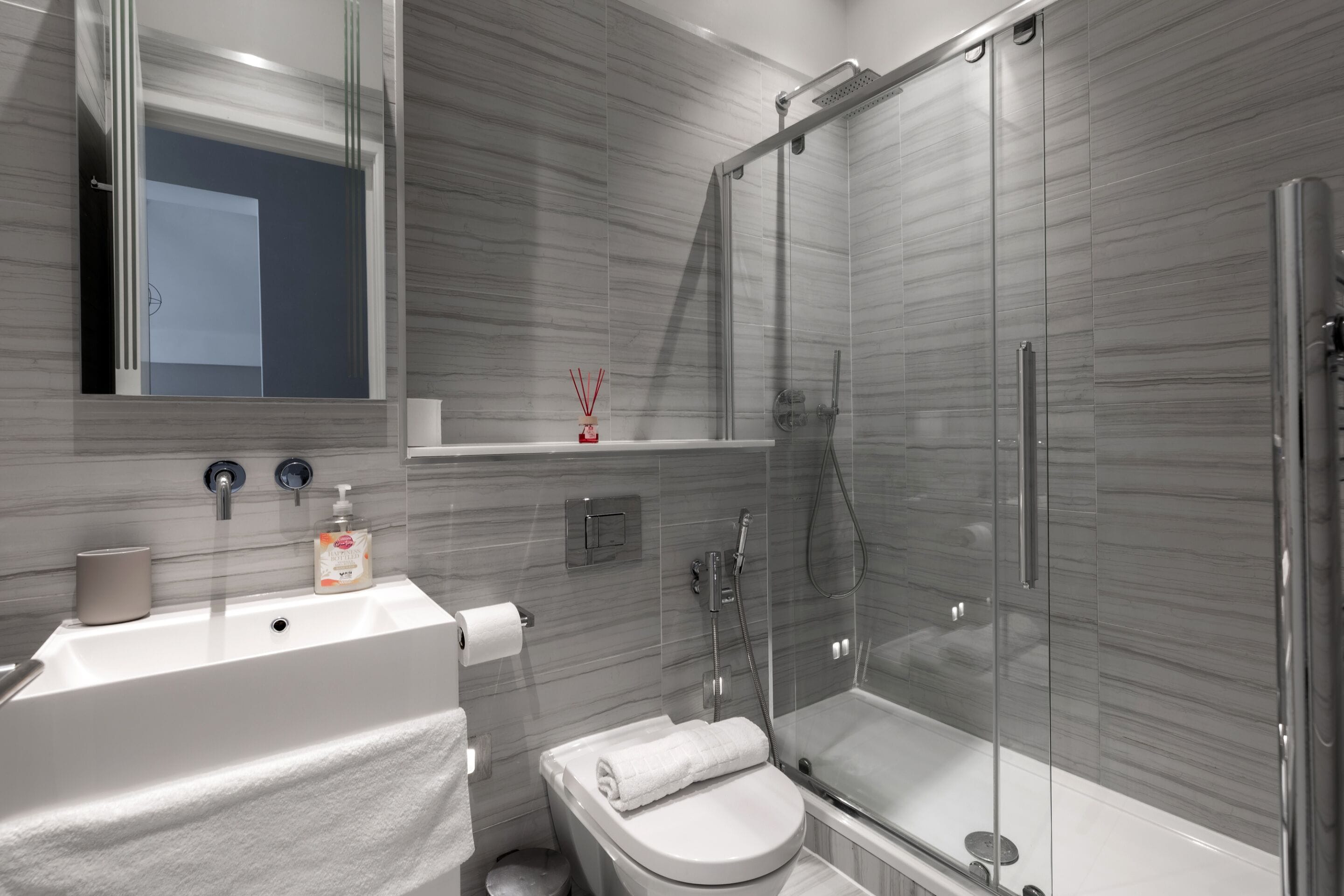 A modern bathroom with a white sink, toilet, and glass-enclosed shower.