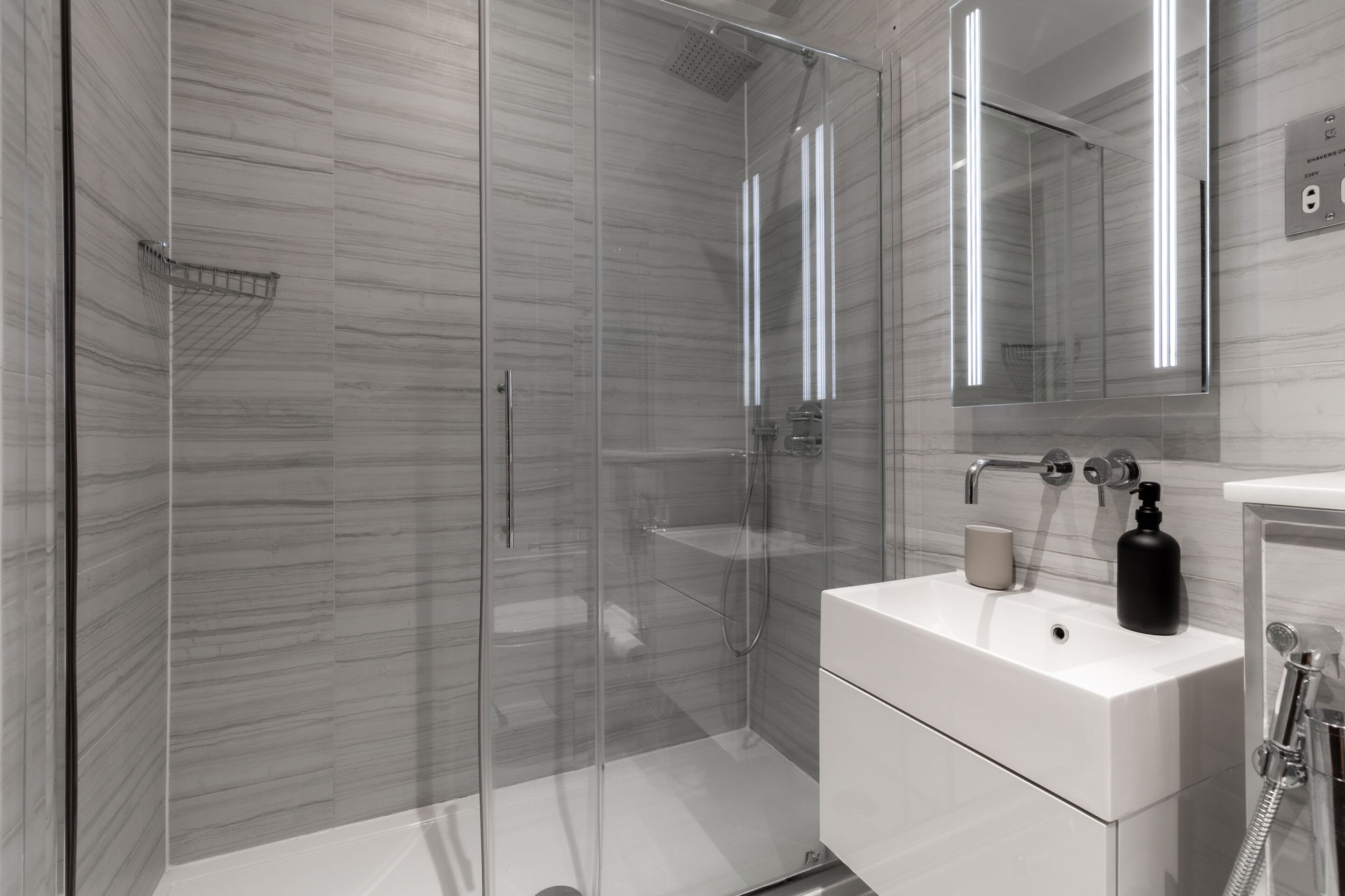 A modern bathroom with a glass-enclosed shower, a white sink, and a mirror above it.