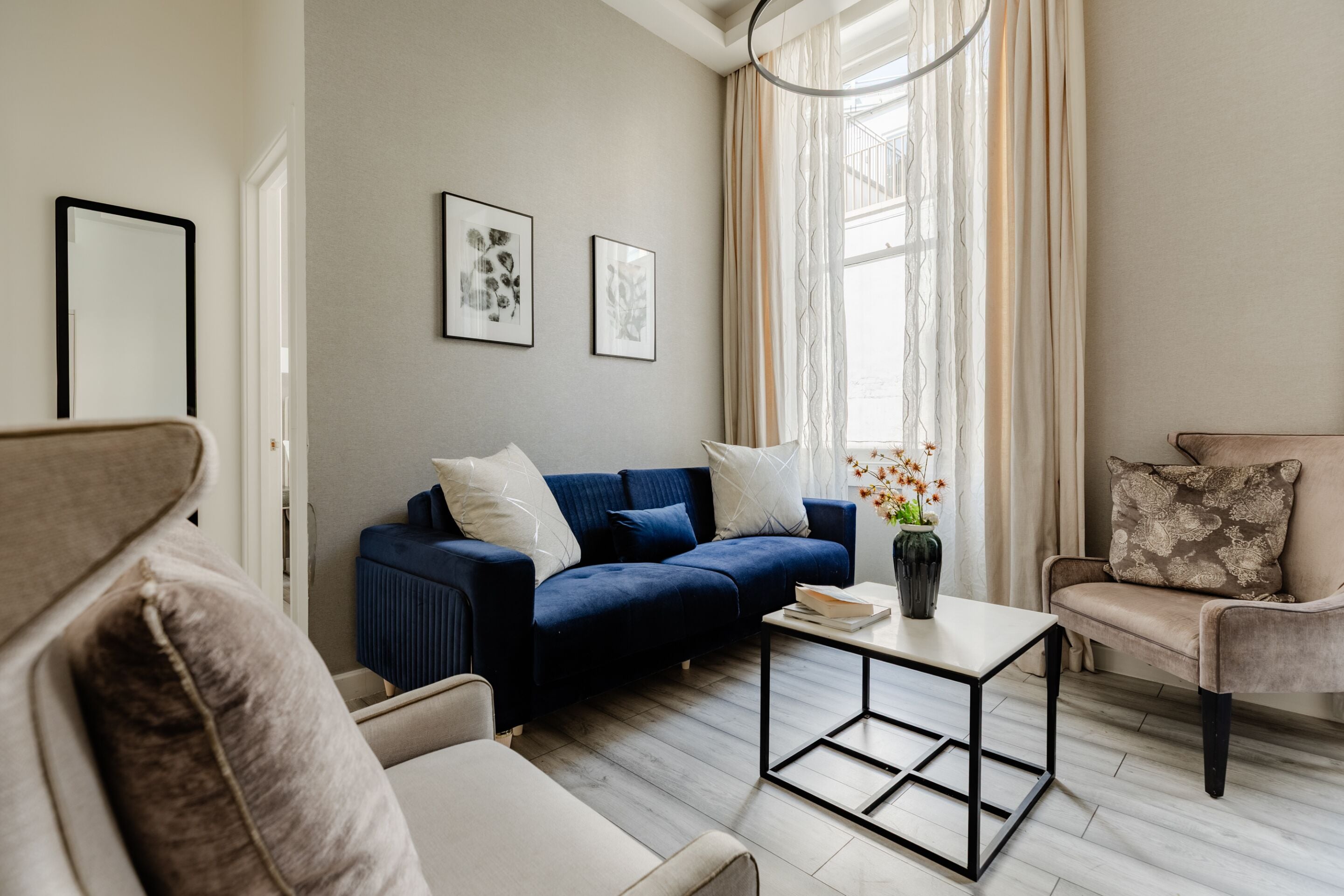 Una sala de estar moderna con un sofá azul, sillones color beige, una mesa de centro y obras de arte en las paredes.