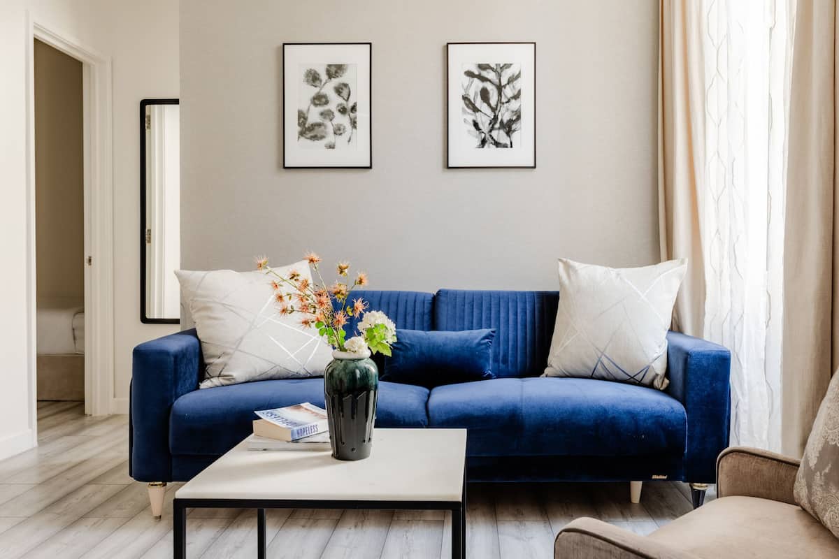 Un salon avec un canapé bleu, une table basse blanche et un vase rempli de fleurs. Deux tableaux encadrés sont accrochés au mur.