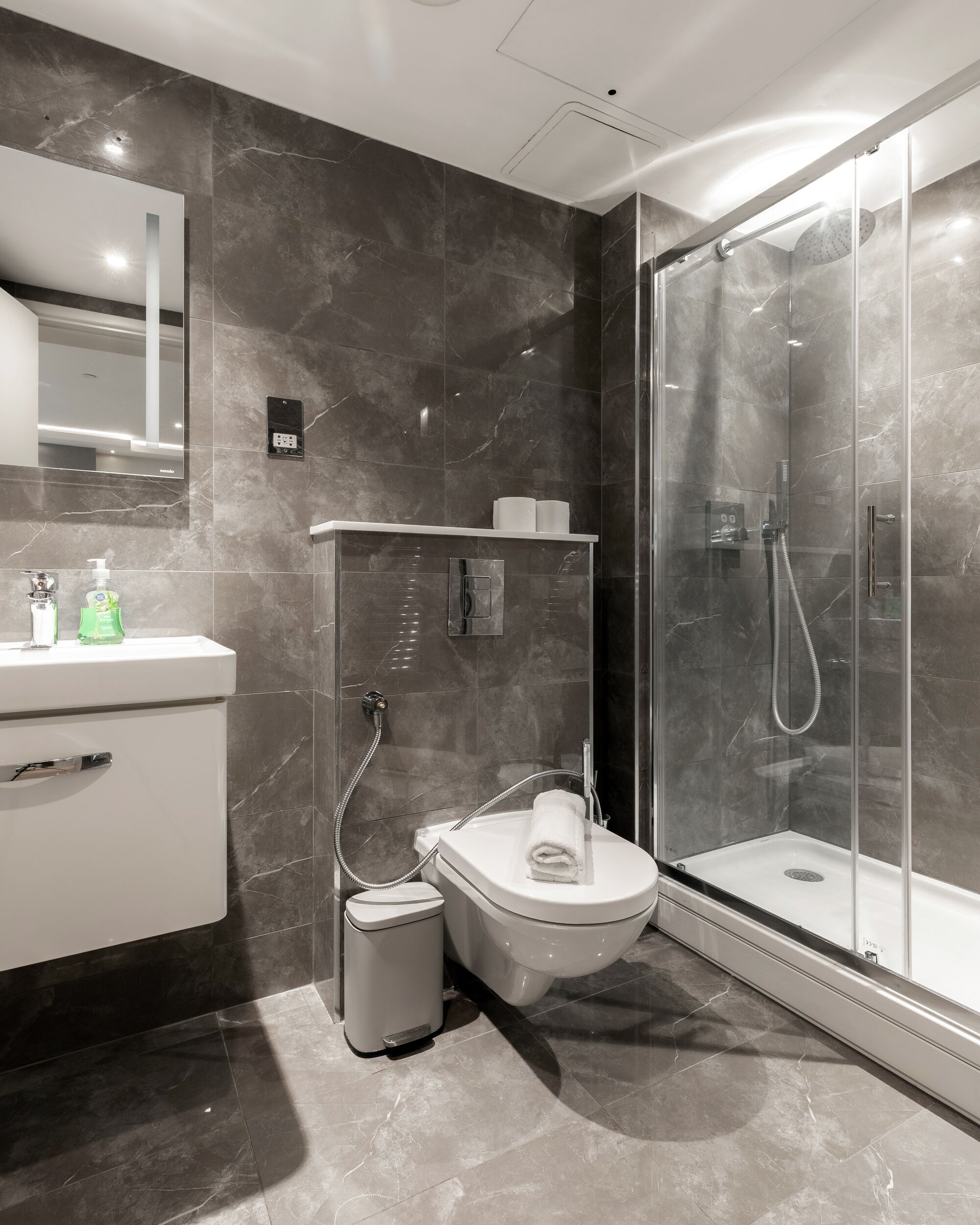 Un bany modern amb dutxa de vidre, un lavabo blanc i un vàter.