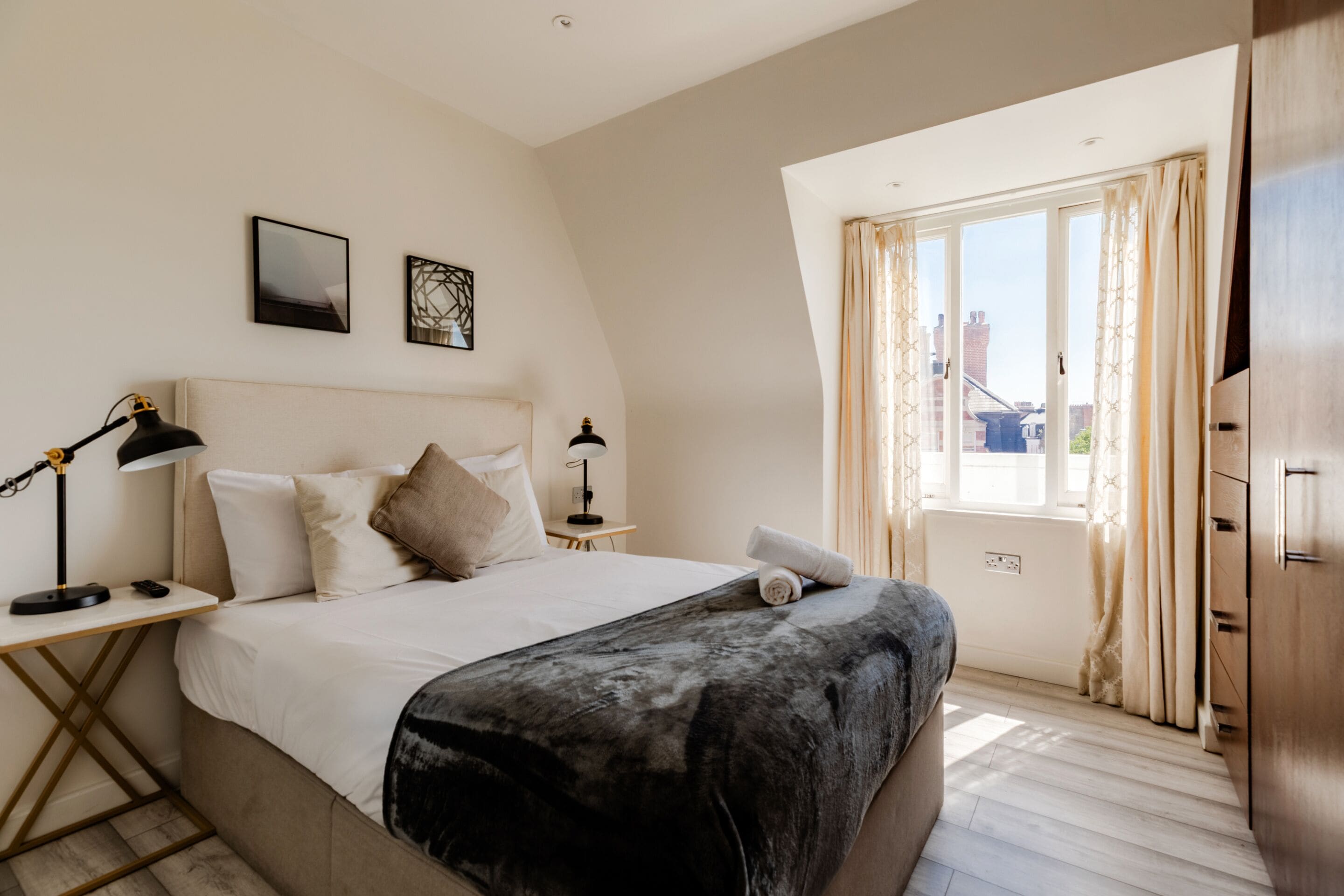 A bedroom with a bed, bedside tables, a lamp, a window with curtains, and a view of the outside.