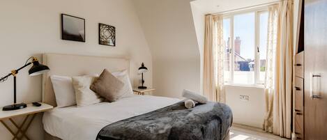 A bedroom with a bed, bedside tables, a lamp, a window with curtains, and a view of the outside.