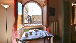 A room with a table set for tea, a view of a city street through an arched window, and a radiator on the wall. - Signoria Farine (Florence)