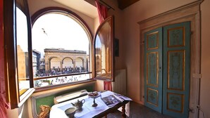 A room with a view of a historical building through a large arched window, a table with a teapot and pastries, and a door with decorative panels. - Signoria Farine (Florence)