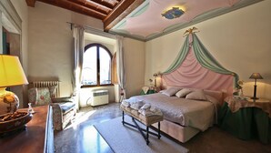A bedroom with a four-poster bed, a wooden bench, a table with a lamp, and a view of the outside through a window. - Signoria Farine (Florence)