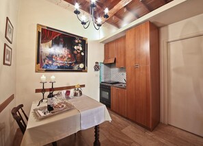 A dining area with a table set for two, a chandelier, wooden cabinets, and a kitchen in the background. - Signoria Farine (Florence)