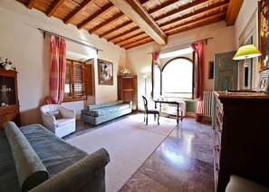 A cozy living room with a wooden ceiling, a sofa, a chair, a table, and a window with curtains. - Signoria Farine (Florence)