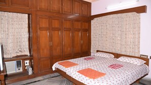 Une chambre avec une grande armoire en bois, un lit avec une literie à motifs floraux et un radiateur placé sous la fenêtre.