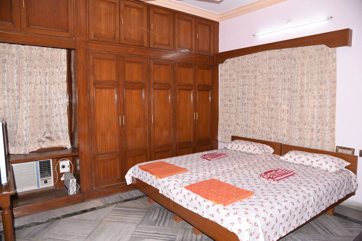 Une chambre avec une grande armoire en bois, un lit avec une literie à motifs floraux et un radiateur placé sous la fenêtre.