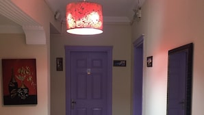 En hall med en lila dörr, en röd brandsläckare och en taklampa.