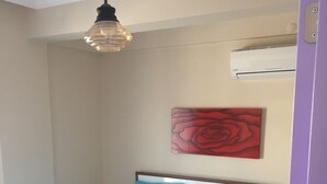 En snyggt bäddad säng med blått och vitt sänglinne, ett konstverk med en röd ros på väggen och en hängande lampa.