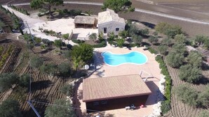 Vista aérea de una propiedad con piscina, un edificio de piedra y un área de patio cubierto.