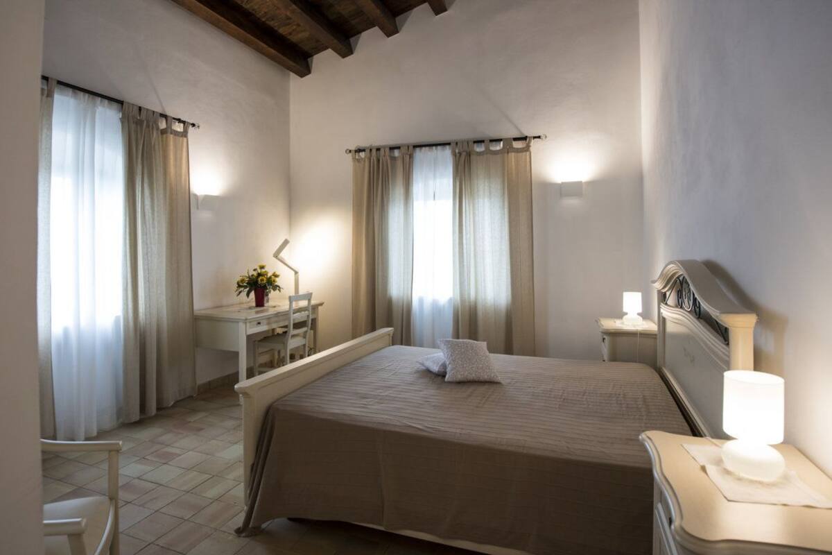 A bedroom with a bed, bedside table, lamp, desk, chair, and curtains.