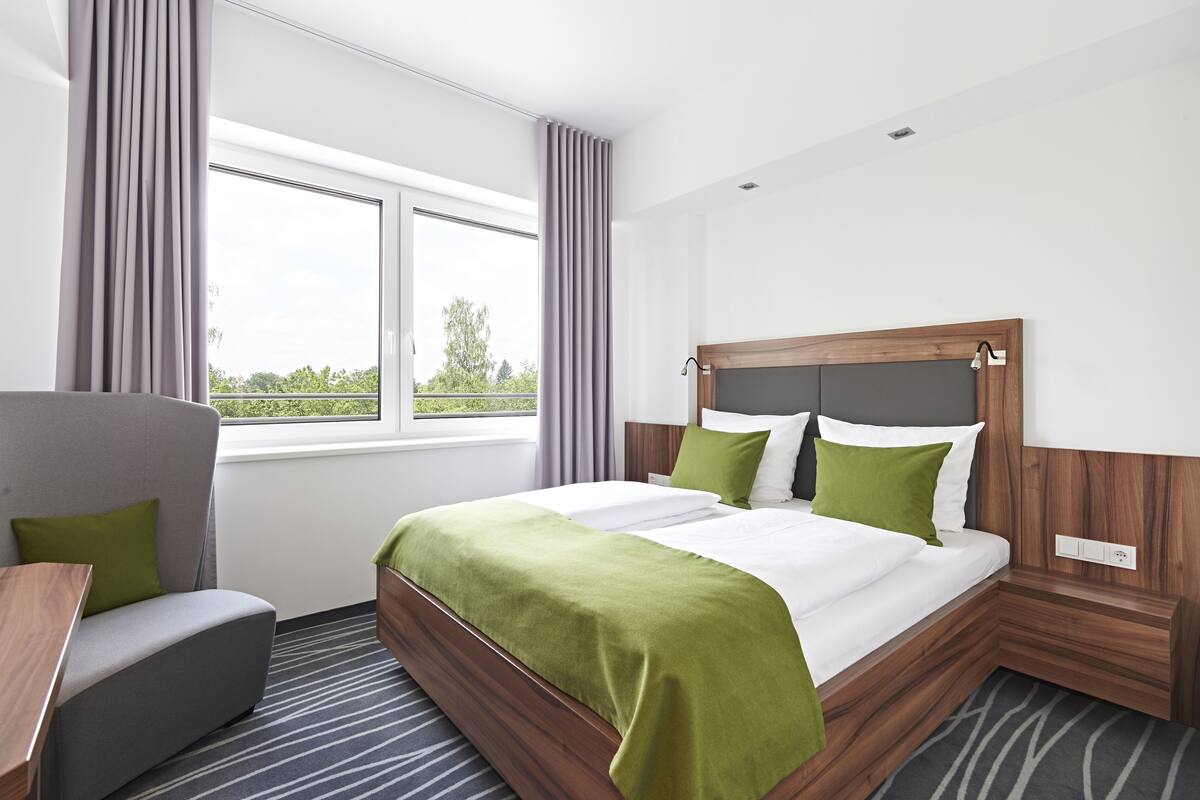 A hotel room with a bed, a chair, a window, and a view of greenery.