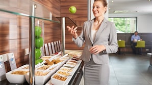 Un espace buffet proposant divers plats, une vitrine réfrigérée contenant des pommes vertes et une personne vêtue d’un costume.