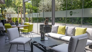 Un espace extérieur moderne aménagé avec des canapés, des fauteuils et des tables, agrémenté d’un panneau avec un code QR et offrant une vue sur la verdure environnante.